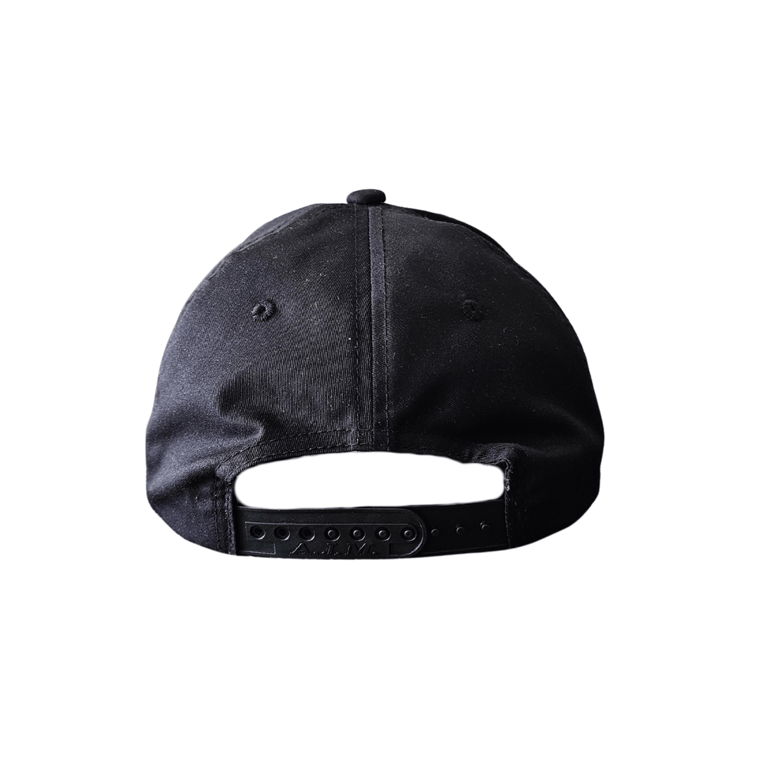 Black snapback hat with white printed Red Rebel Armour crest on front panel, displayed on a wooden table facing backwards.